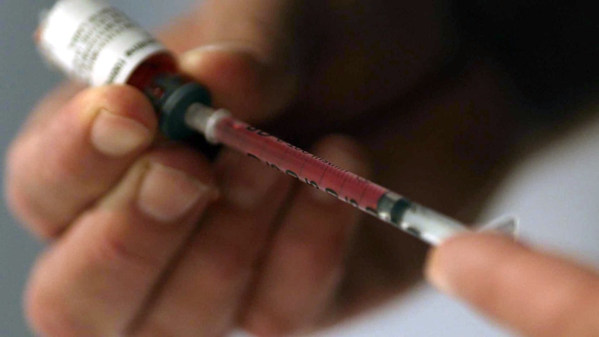 A close up on hands drawing red liquid from a vial into a syringe.