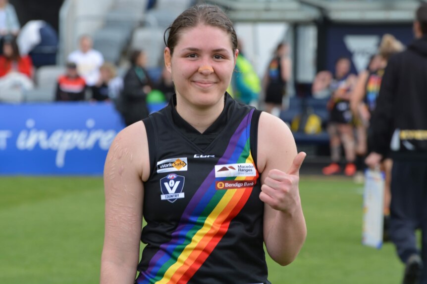 A young woman in a footy singlet smiles for the camera.