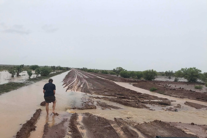 A women treads bare foot though a flooded dirt road