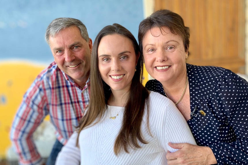 A young woman smiles in between her parents.