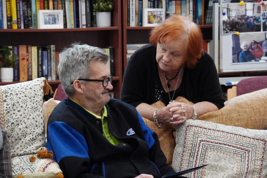 A lady talks to a man in front of a book case