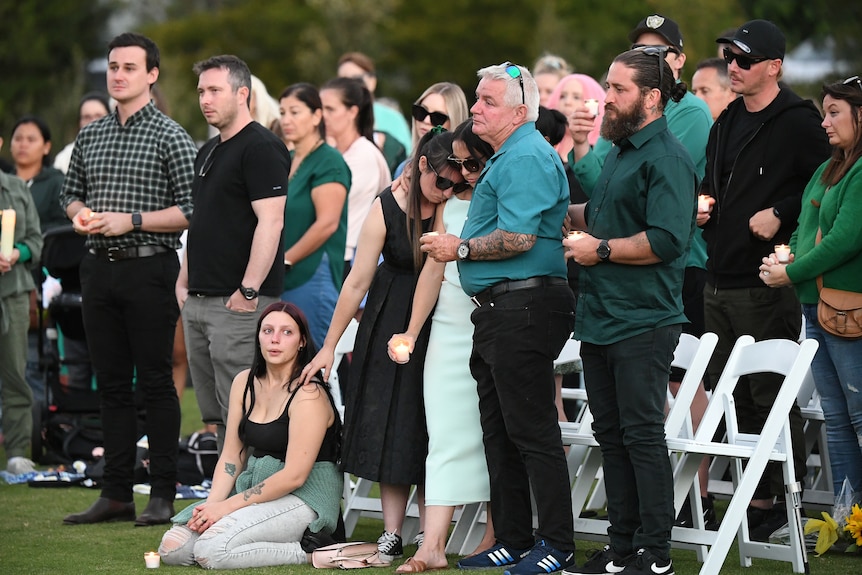 Kelly's father and sisters are seen comforting each other among a crowd of people.