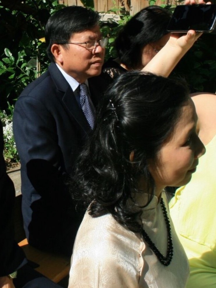 A man of Vietnamese appearance in a suit and tie stands next to a woman of Vietnamese appearance with black hair and white dres.
