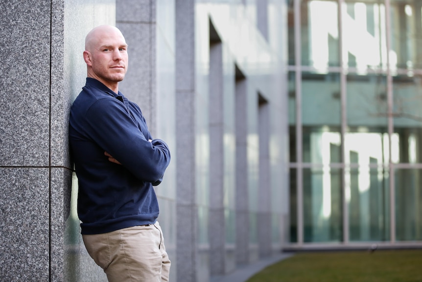 Man wearing dark jumper leaning against building. 