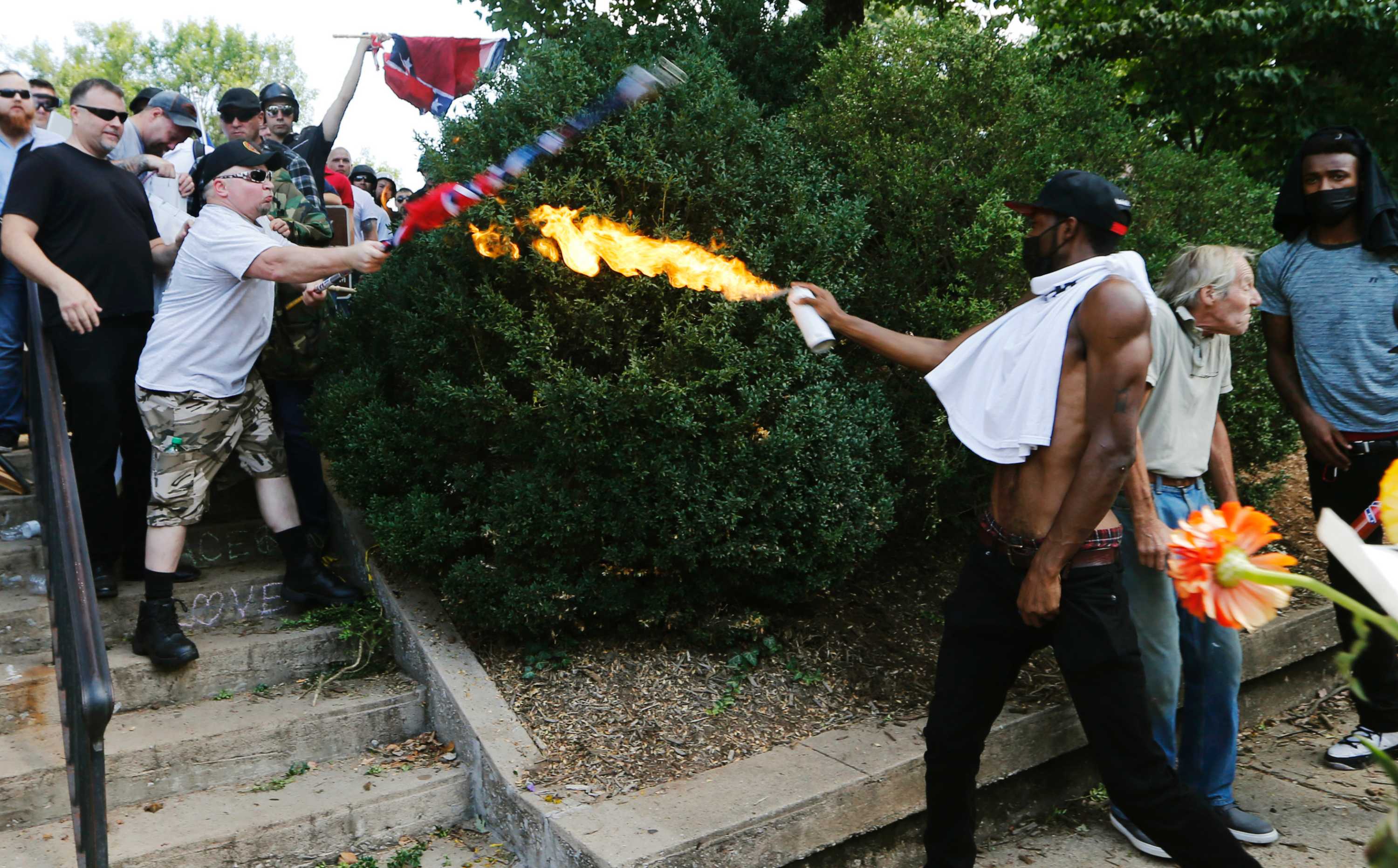 A man directs a lighted spray can at a white nationalist demonstator.