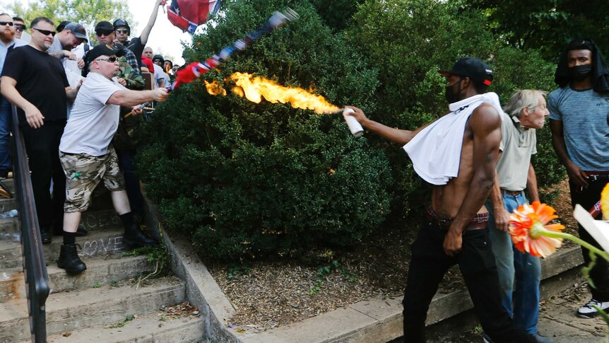 A man directs a lighted spray can at a white nationalist demonstator.