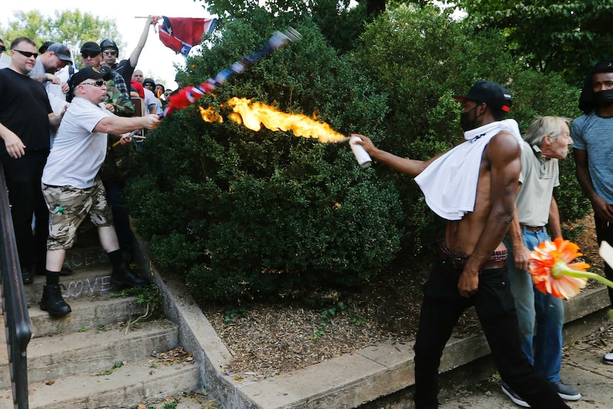 A man directs a lighted spray can at a white nationalist demonstrator.