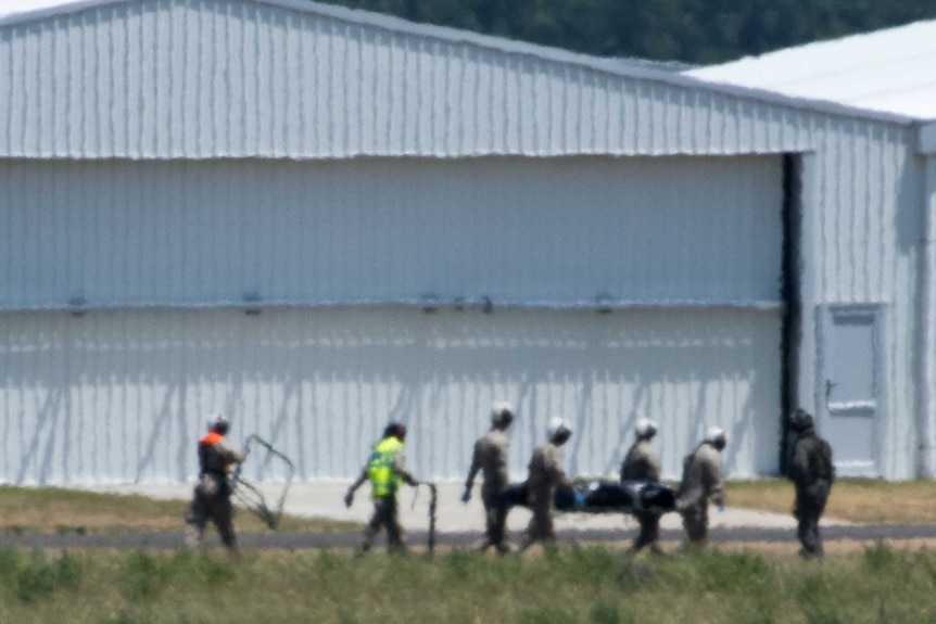 People carry a body on a stretcher outside a large white building