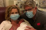 A masked woman and man in hospital, two premature babies are on the woman's chest in a blanket.