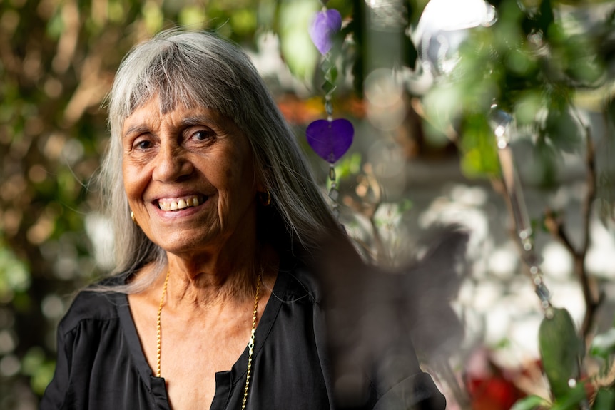 Elderly woman smiling outdoors on a sunny day. 