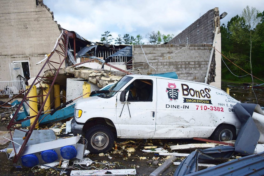 A crushed van sits in front of a heavily damaged shop.