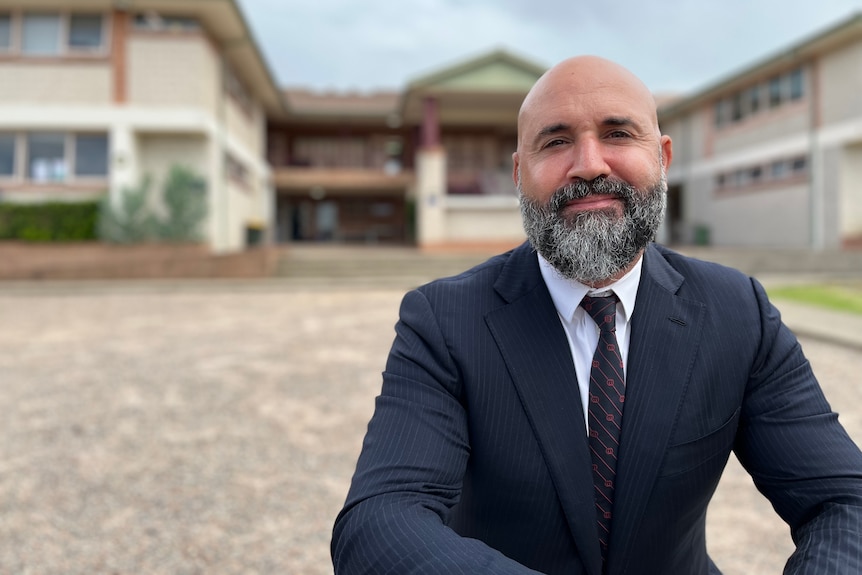 A bald man with a beard wearing a suit in a school environment.