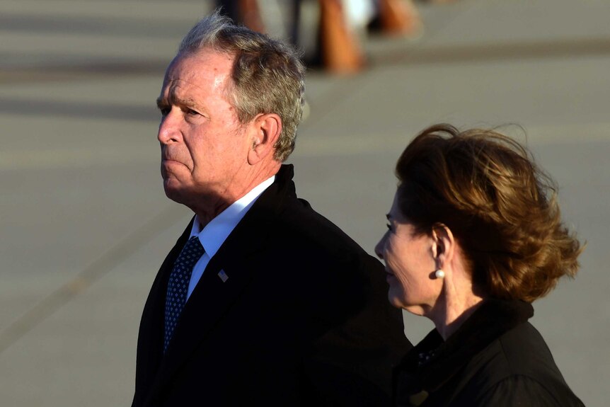 George W Bush, with a sad look on his face, walks alongside his wife Laura Bush.