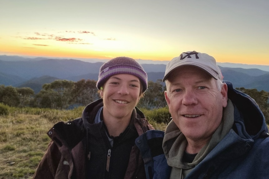 A boy and his dad smiling together while on a mountain.