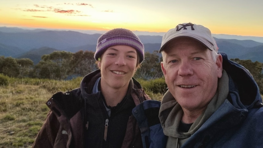 A boy and his dad smiling together while on a mountain.