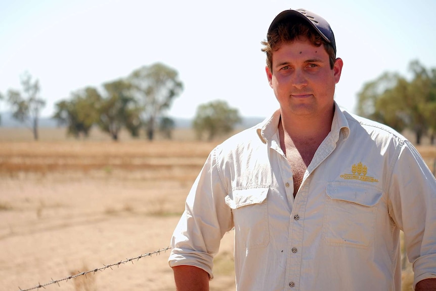 A man with a cap standing in front of a dry paddock