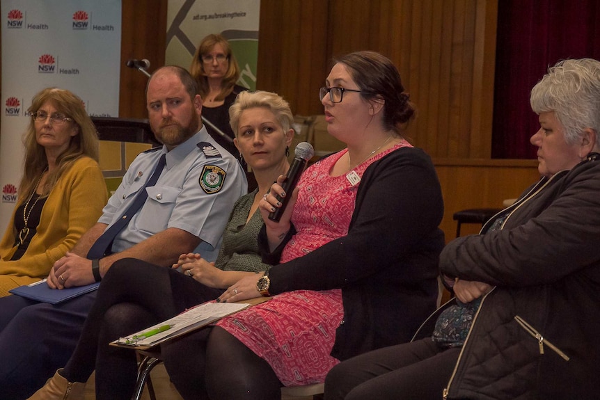 a row of people including a police officer sitting, one woman speaking into a microphone