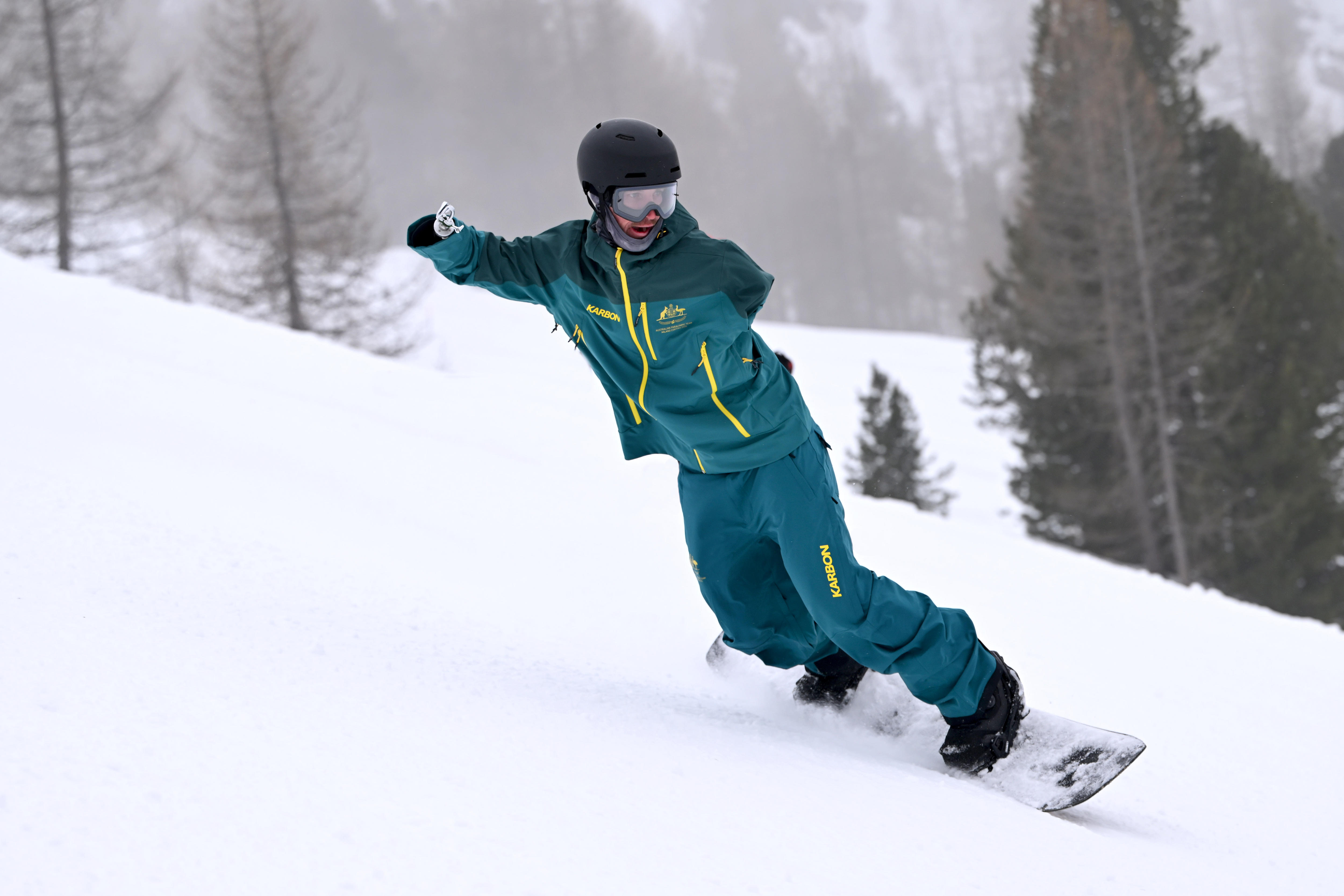 Um snowboarder vestindo verde e dourado está se inclinando para uma curva nas encostas