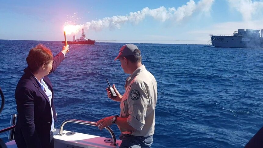 Leanne Enoch holds a flare in front of  ex-HMAS Tobruk