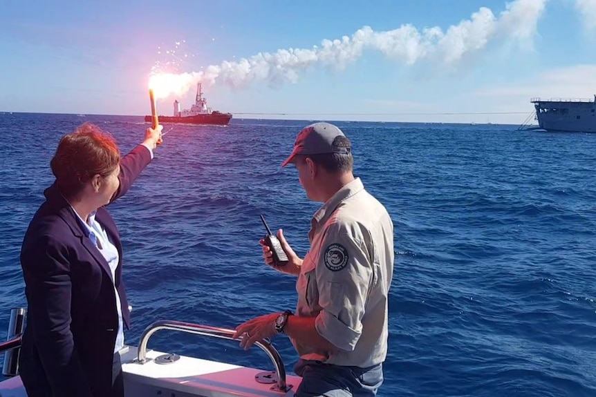 Leanne Enoch holds a flare in front of  ex-HMAS Tobruk