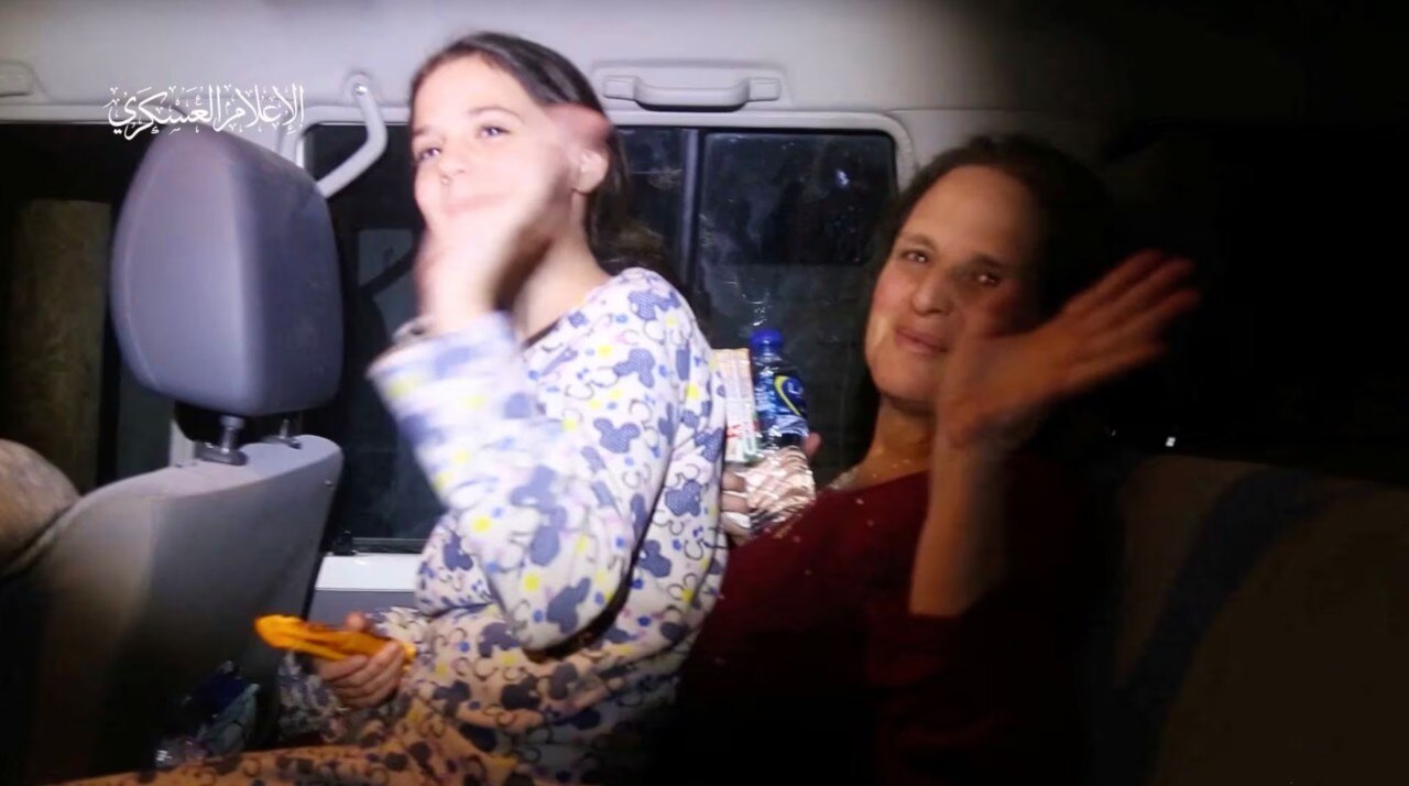 A young girl and a woman can be seen smiling and waving inside a large car