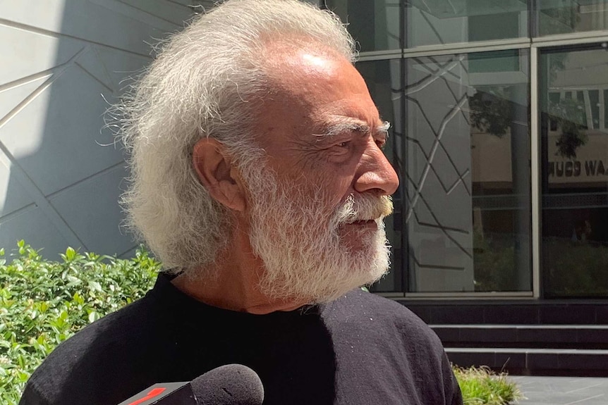 A head and shoulders shot of an older man with white hair and a white beard outside court.