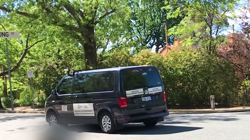 A black patrol van travels down a leafy street.