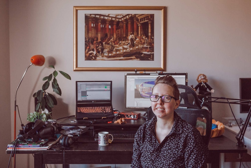 A person sits in a room in front of a laptop and screen