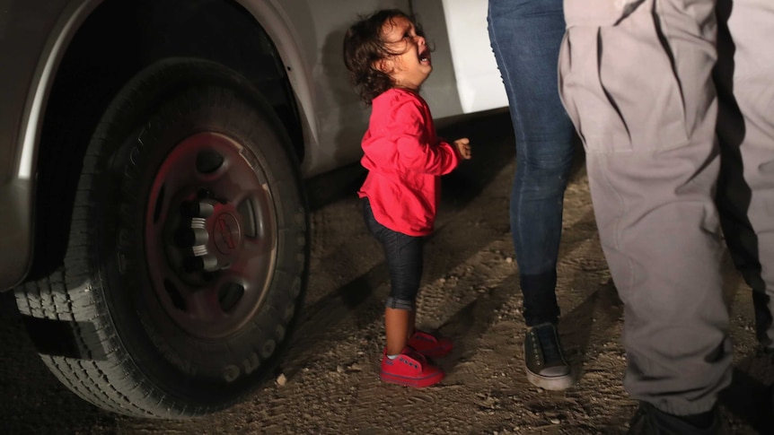 A child cries as her mother is searched on the US-Mexico border