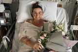 Woman lays in hospital bed, smiling and holding a bouquet of flowers