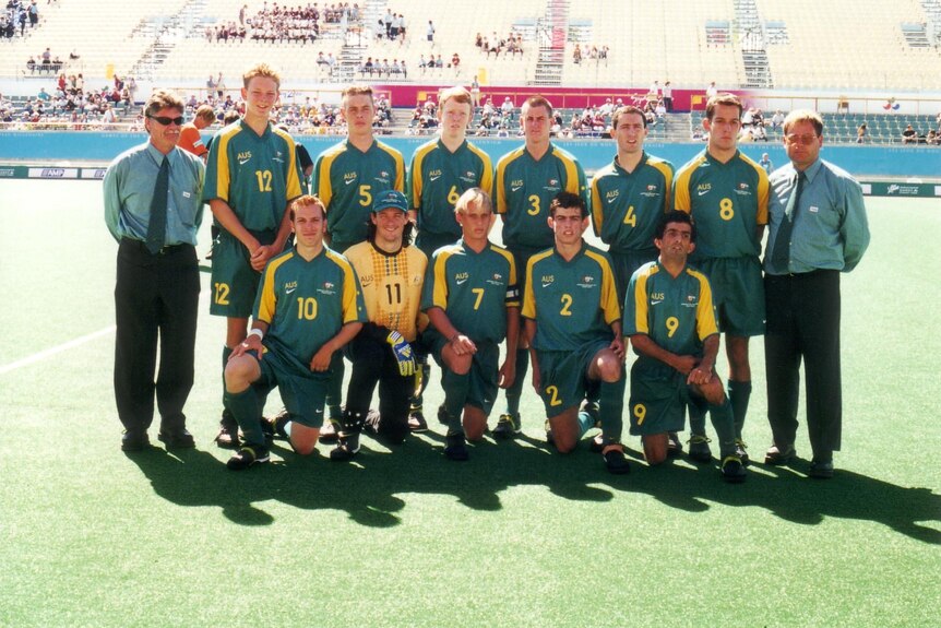 A soccer team wearing green jerseys with yellow sleeves pose for a team photo on a football pitch.