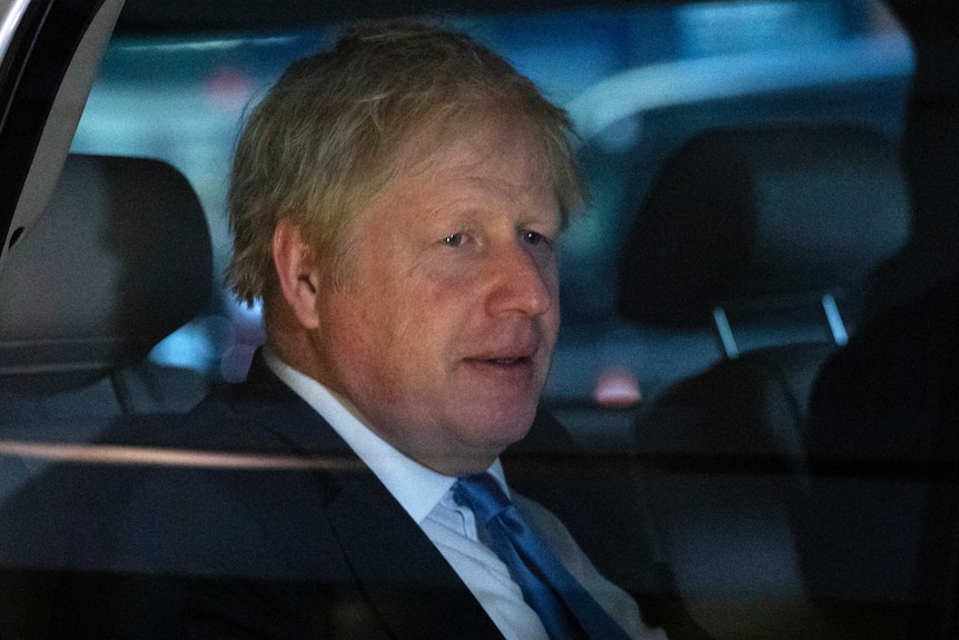 Boris Johnson looks straight ahead as he sits in the back of a car. He has a worried expression on his face and wears a suit.