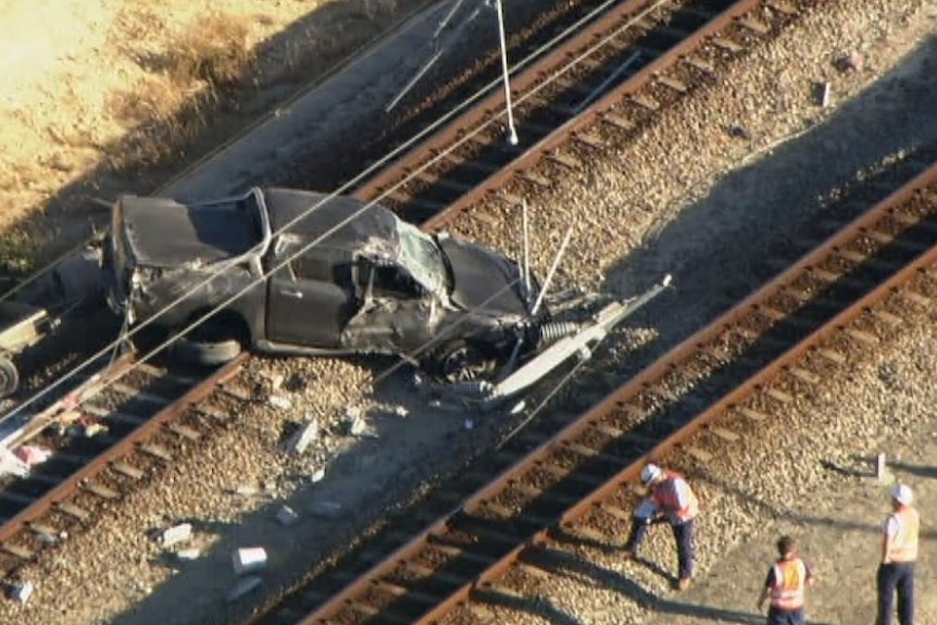 The car, a ute, lies on the tracks. The windscreen is smashed and the driver's side door is damaged. A back wheel has come off.