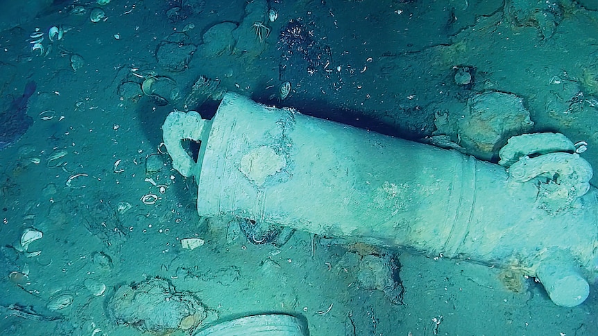  A cannon lying on the ocean floor with bits of debris around it.