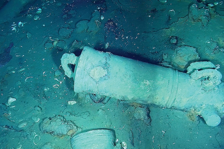  A cannon lying on the ocean floor with bits of debris around it.
