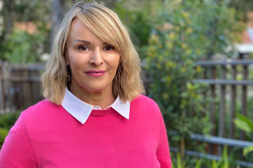 Melanie Anderson smiles wearing a pink jumper.