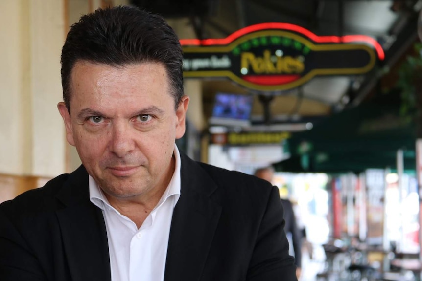 Nick Xenophon stands outdoors with a pokies sign in the background.