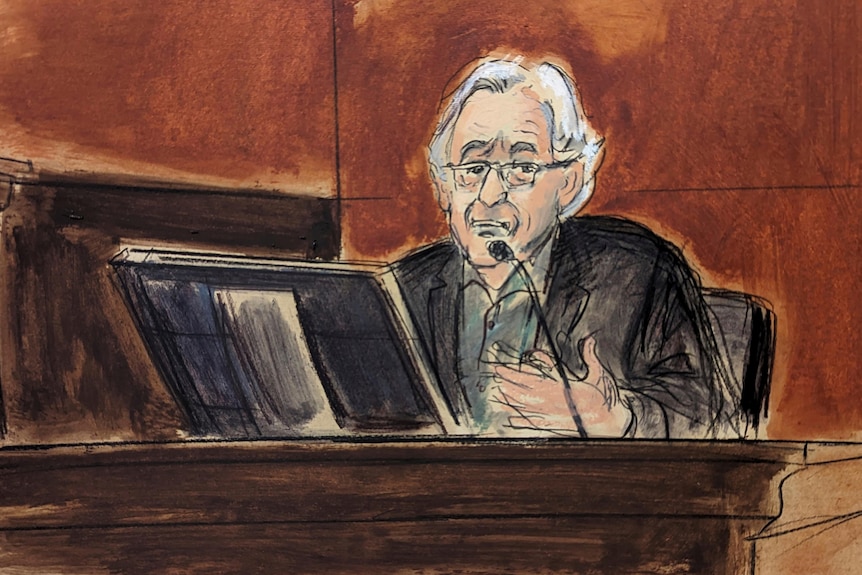 A court sketch of a white-haired man wearing glasses seated in a witness box behind a microphone.