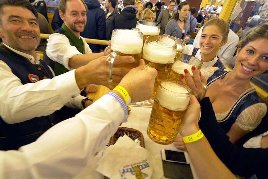 A group of people smile and clink their beers together at Oktoberfest.