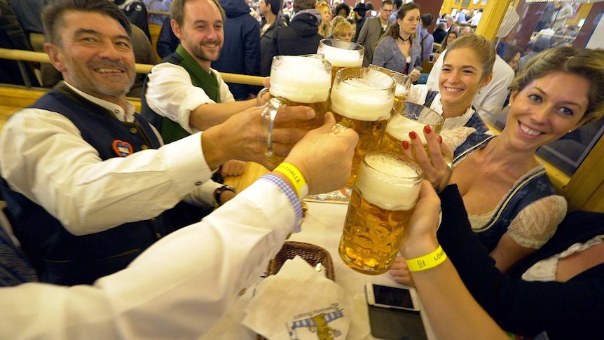 A group of people smile and clink their beers together at Oktoberfest.