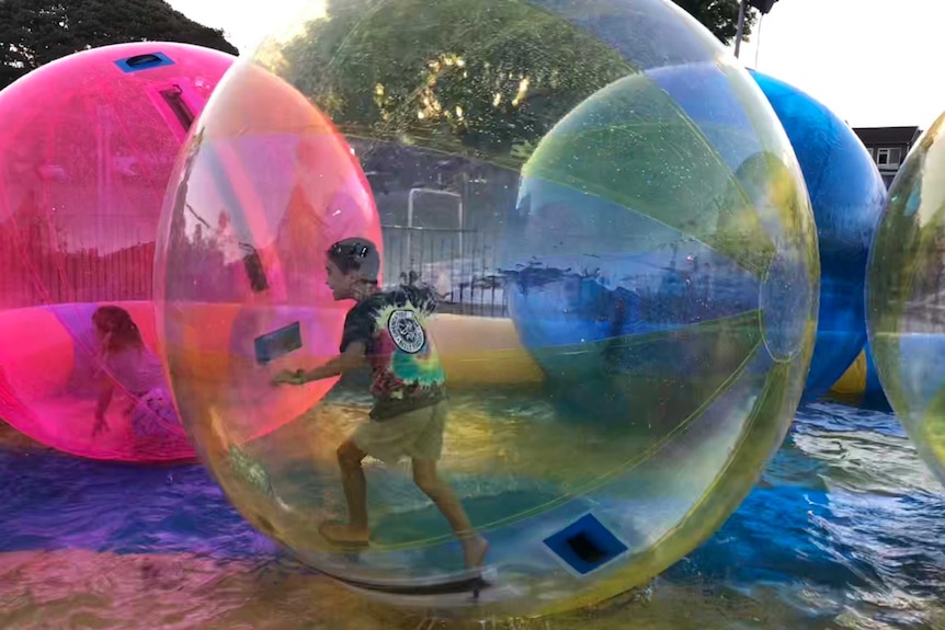 A child runs inside a giant inflatable ball floating on the water.