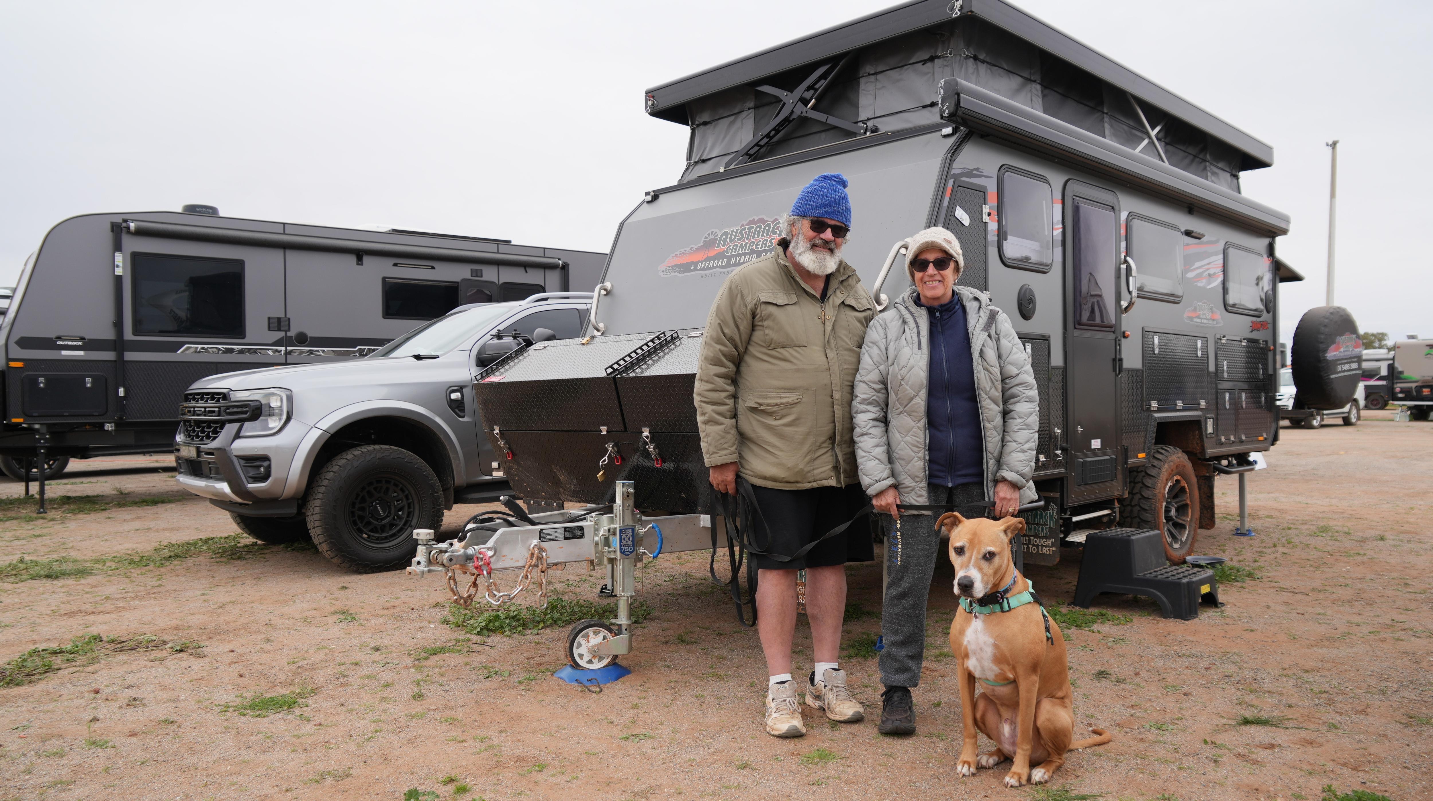Man and woman stand in front of a caravan with a dog