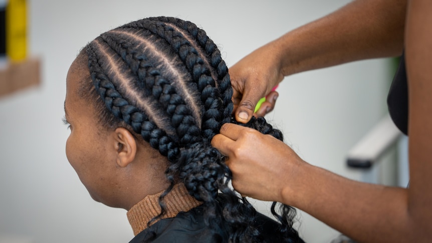 A hairdresser braids a woman's hair.