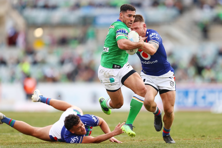 Canberra Raiders player Jamal Fogarty runs past two Warriors defenders with the ball in hand.