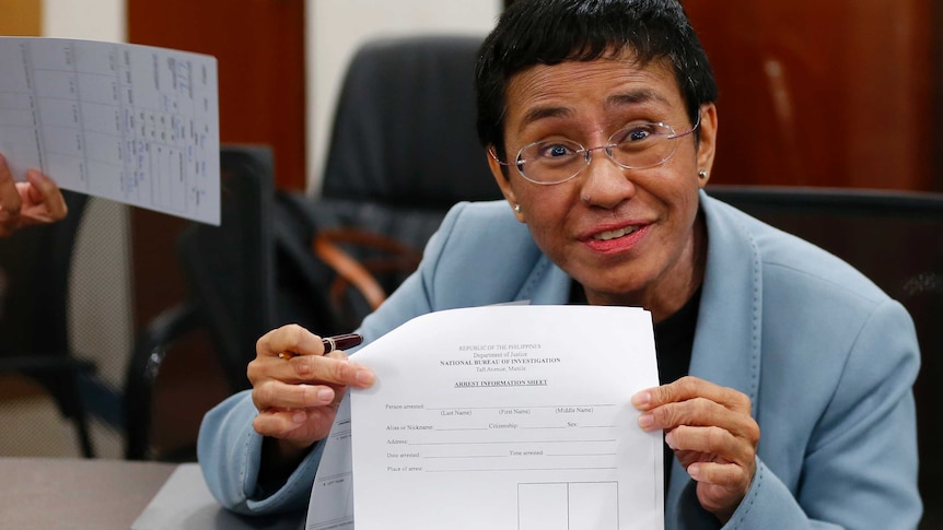 A woman wearing a blue jacket  shows an arrest form after being arrested by the National Bureau of Investigation in Manila.