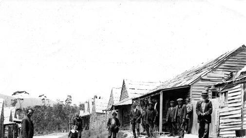 Old photograph of men standing in street outside wooden houses