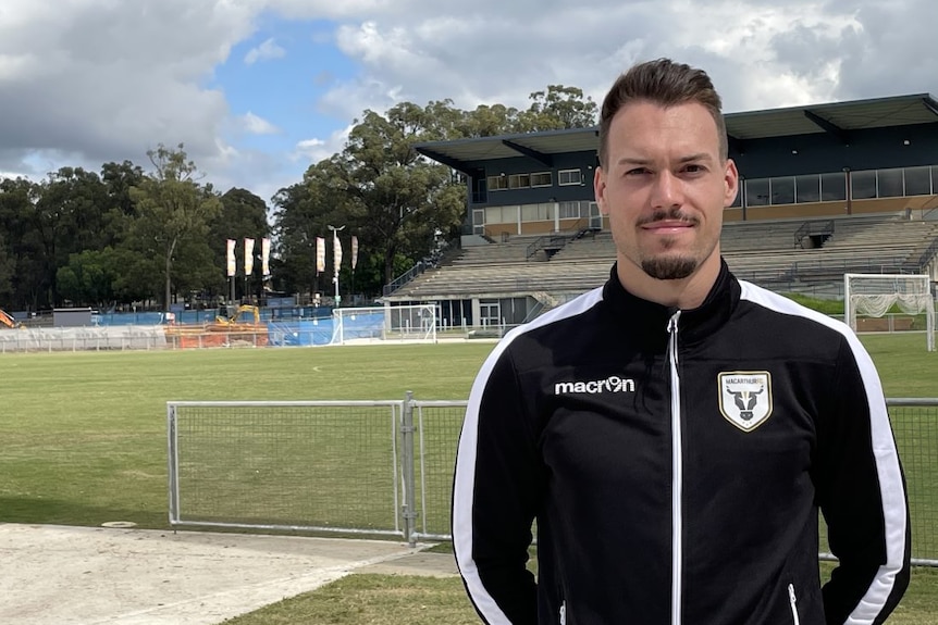 A soccer player poses for a picture in front of a football stadium.