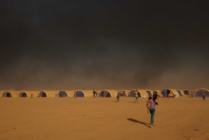 Smoke rising over rows of tents from oil fields in the distance.