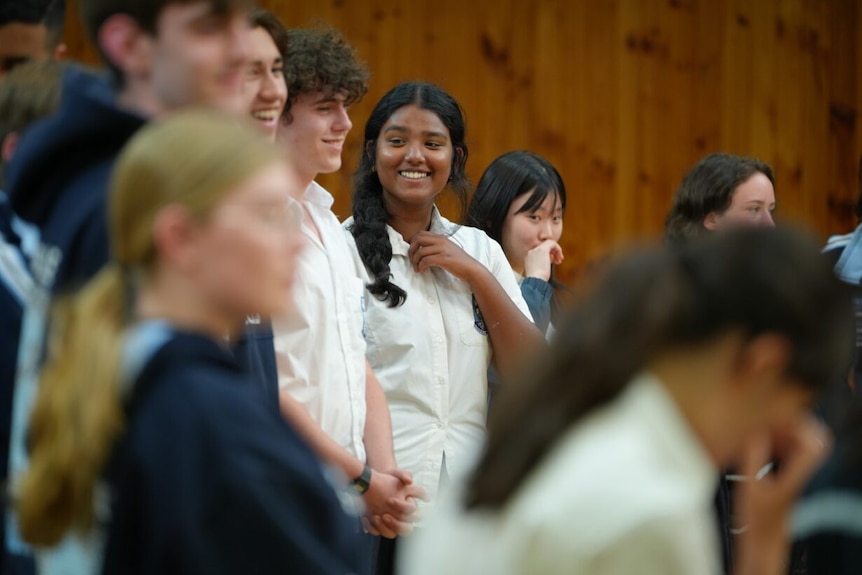 Girl in school uniform smiles while standing in between other school students singing in a choir.