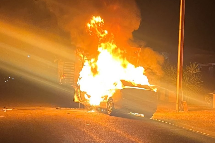 A car on a road with flames engulfing it and smoke billowing into the air